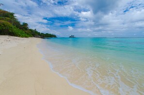 Di pantai, pasir putih, kursi berjemur, dan payung pantai