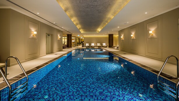 A hotel swimming pool with a blue mosaic floor, lounge chairs, and wall-mounted lights. - Herbert Samuel Jerusalem (Jerusalem)