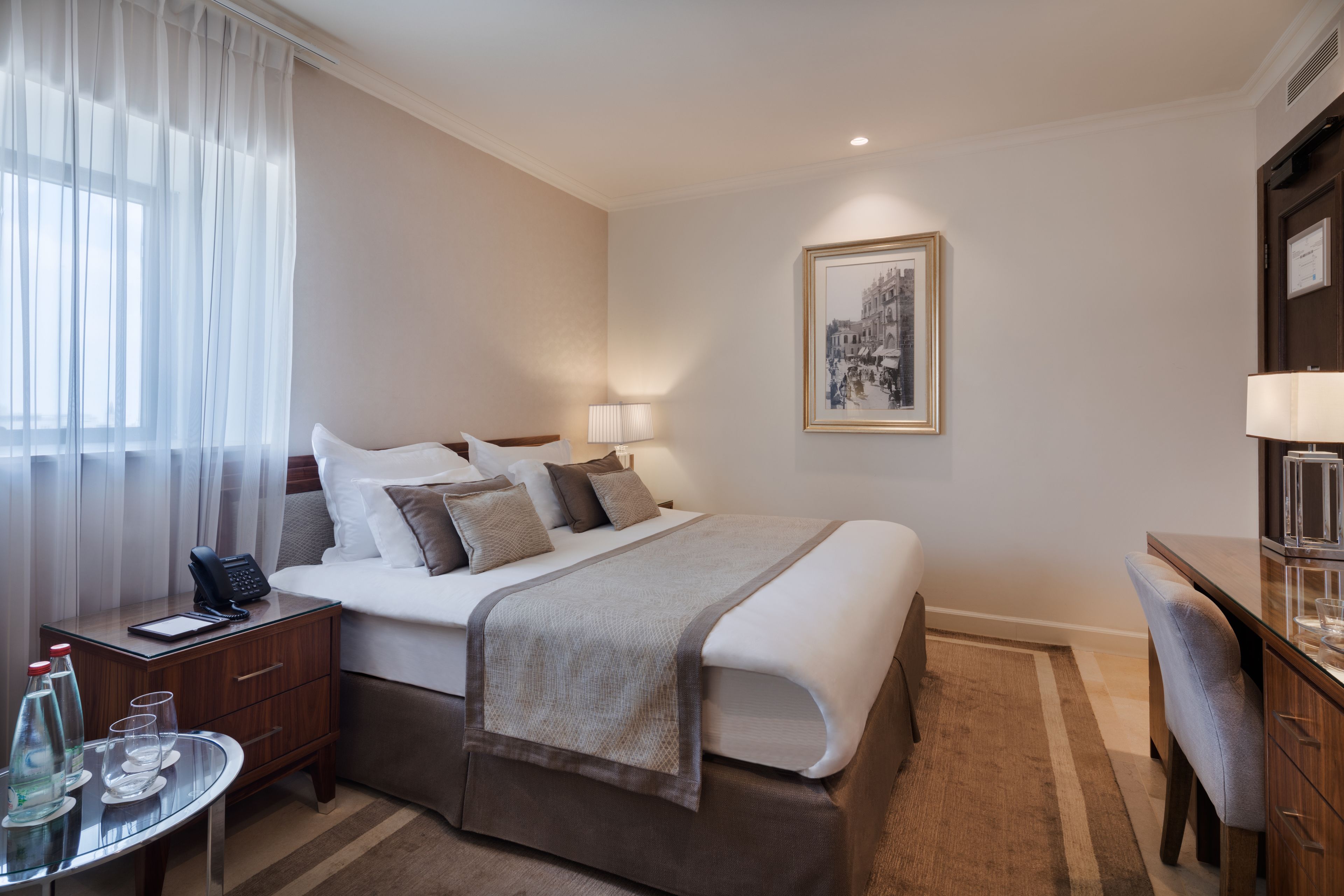 A hotel room with a bed, bedside table, lamp, and a framed picture on the wall.