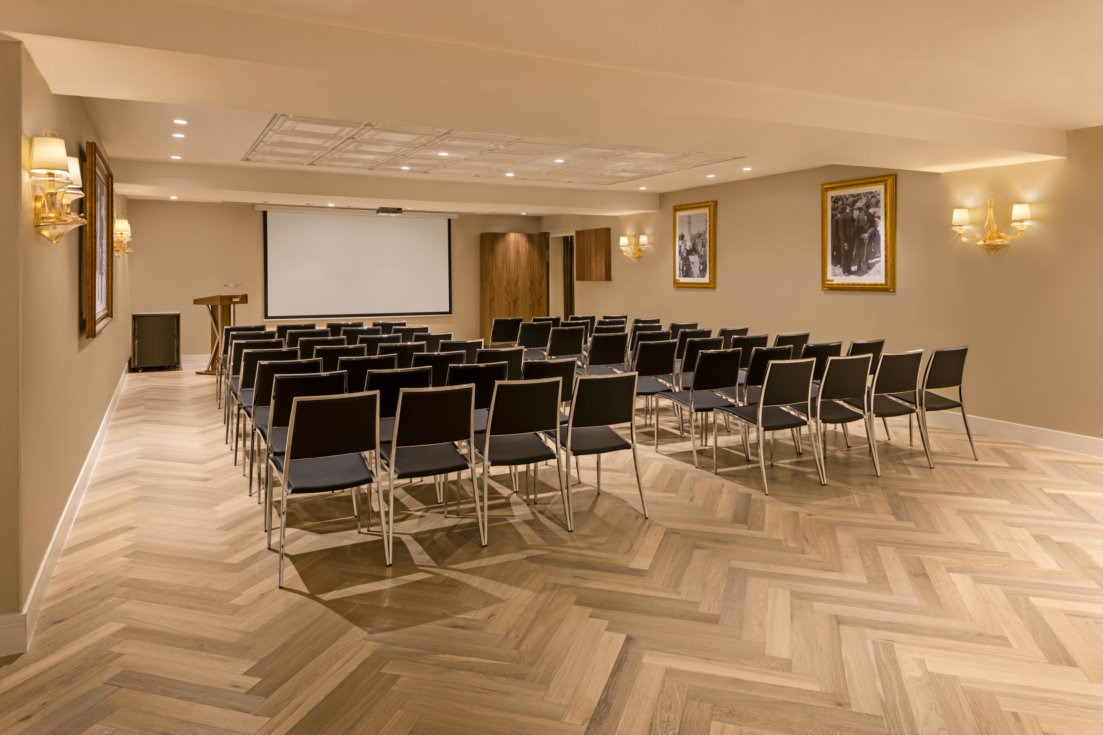 A conference room with a large screen, rows of chairs, and a podium.