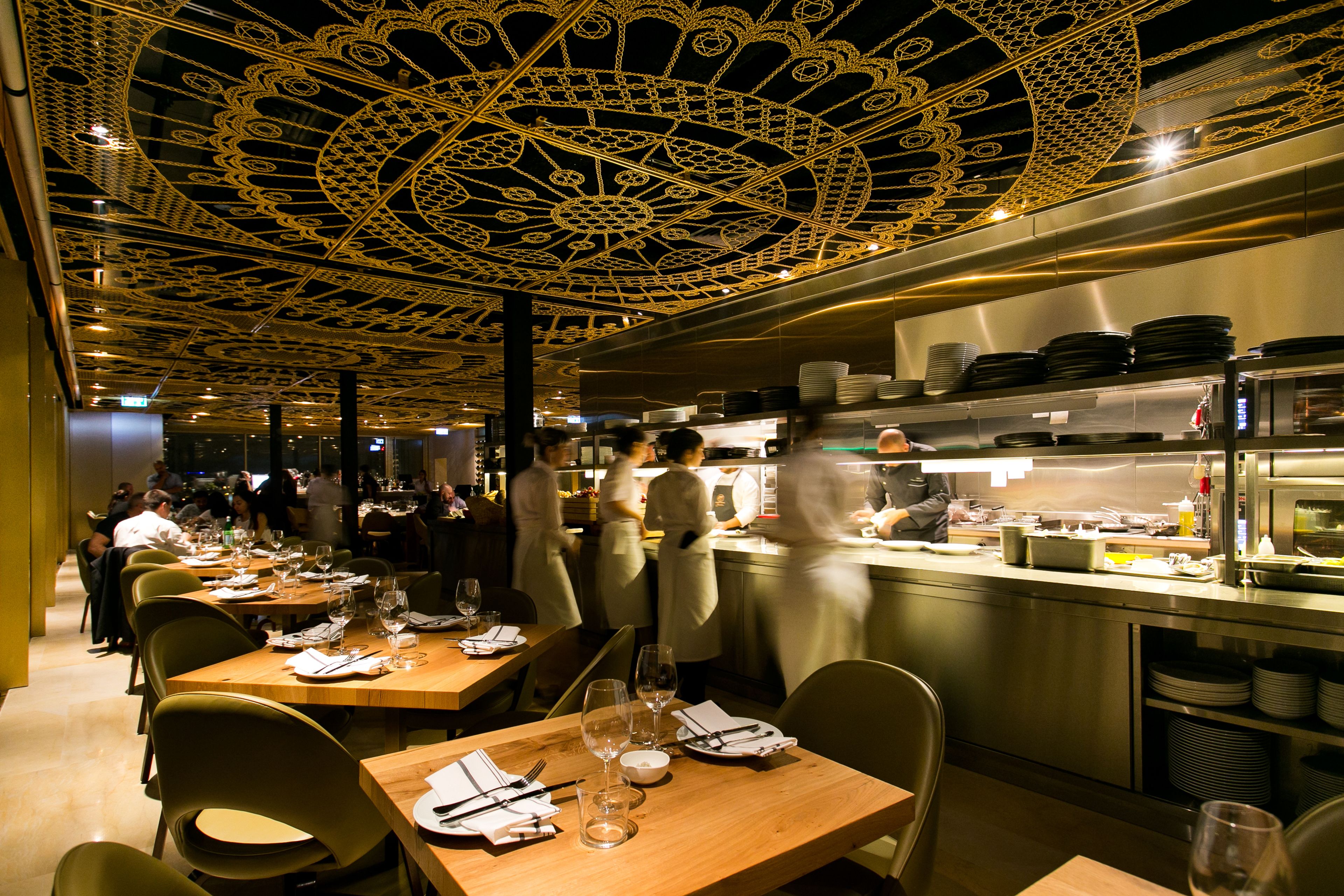 Un restaurant doté d’une grande salle à manger, avec de nombreuses tables dressées, où l’on trouve des assiettes, des verres et des couverts.