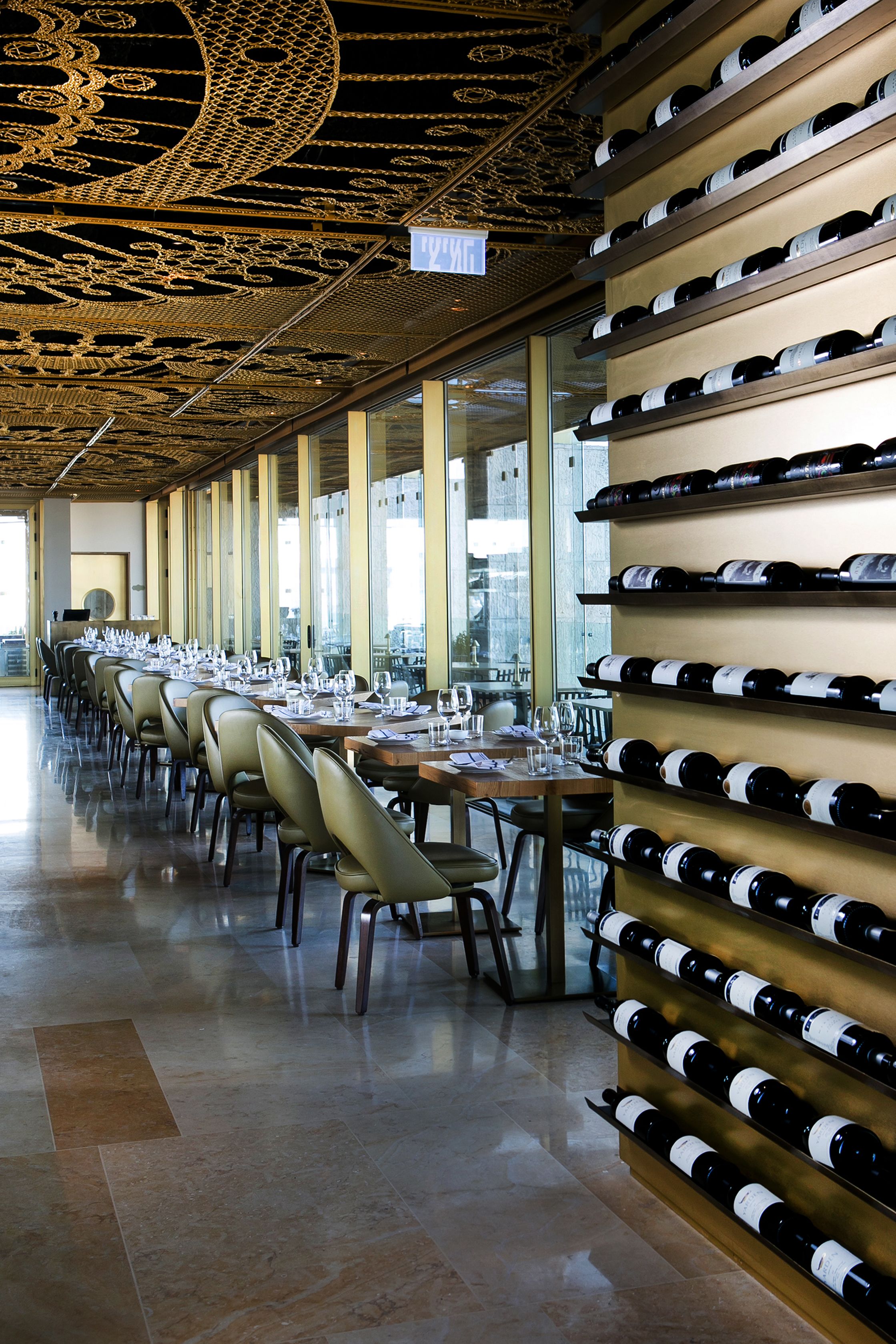 A restaurant with long tables set for dining, a wine rack on the wall, and a decorative ceiling.