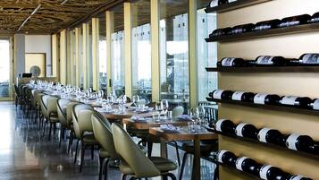 A restaurant with long tables set for dining, a wine rack on the wall, and a decorative ceiling.