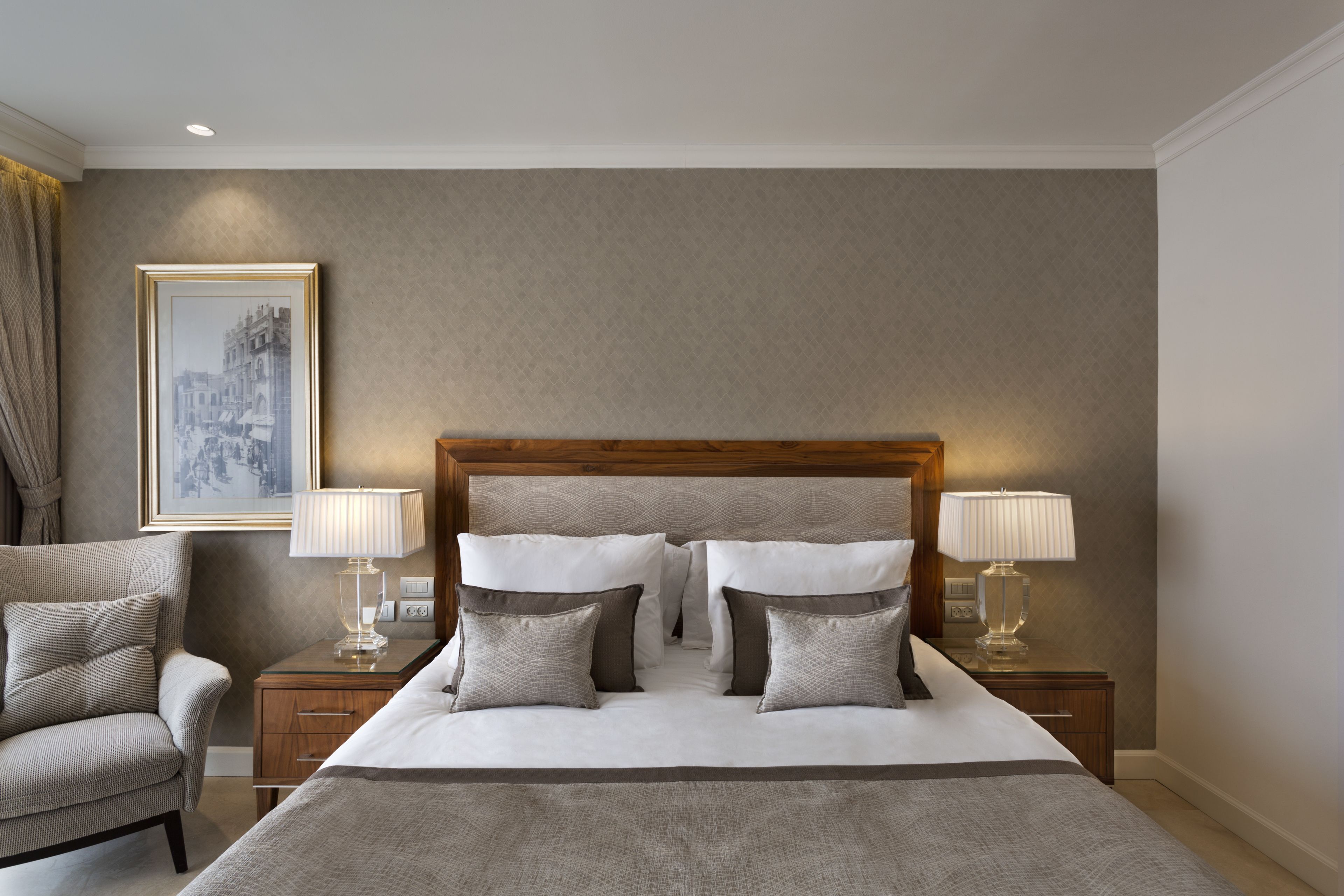 A hotel room with a large bed, two bedside tables with lamps, a chair, and a framed picture on the wall.