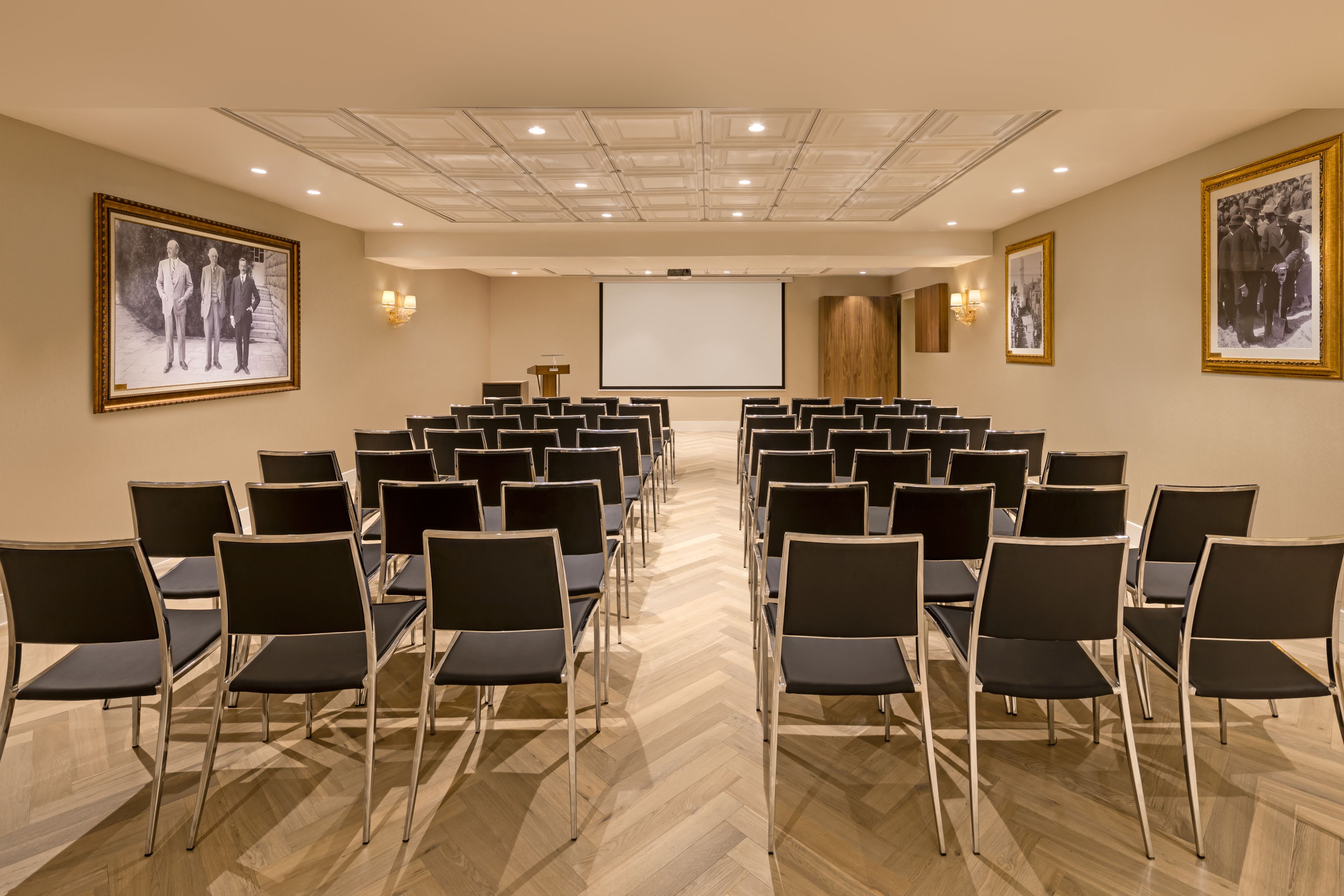 A conference room with rows of chairs, a projector screen, and framed pictures on the walls.