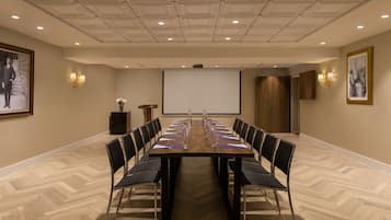 A conference room with a long table, chairs, a projector screen, and framed pictures on the walls.