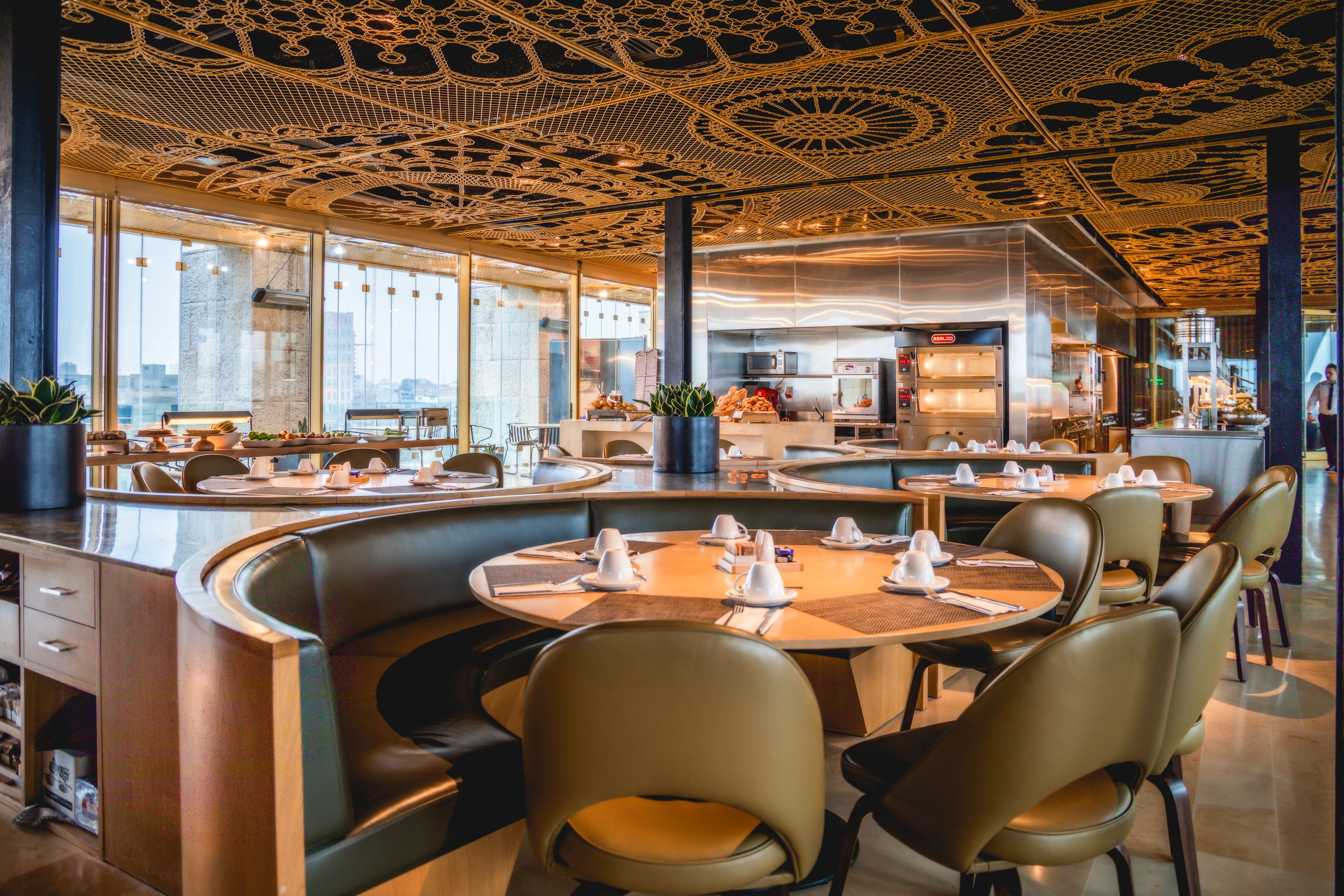 A modern restaurant with round tables, leather booths, and a ceiling with intricate patterns.