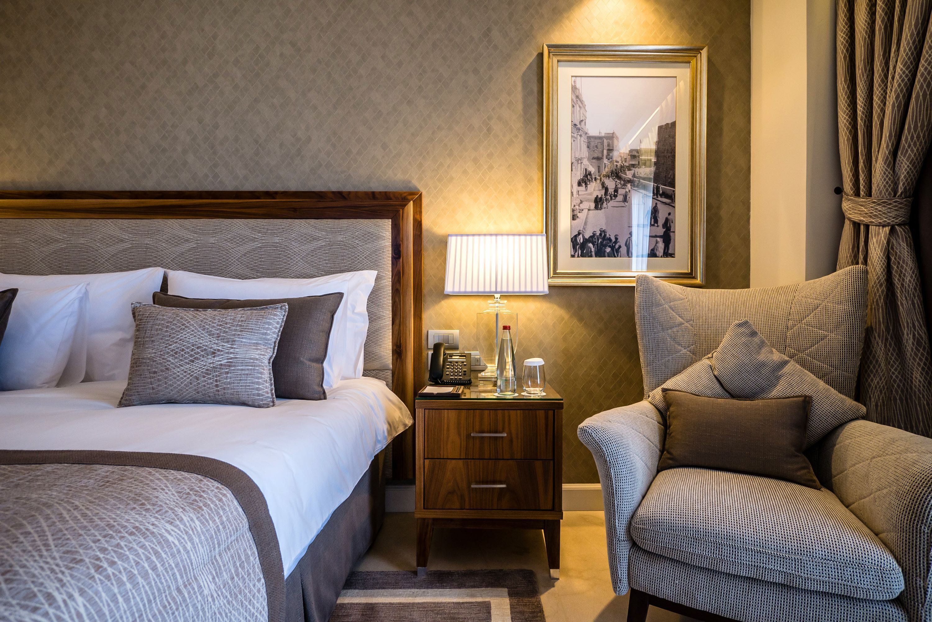 Ein Hotelzimmer mit einem großen Bett, einem Nachttisch mit Lampe, einem gerahmten Bild an der Wand und einem Sessel.