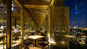 An indoor dining area with tables and chairs, large windows, and a city view at night. - Herbert Samuel Jerusalem (Jerusalem)