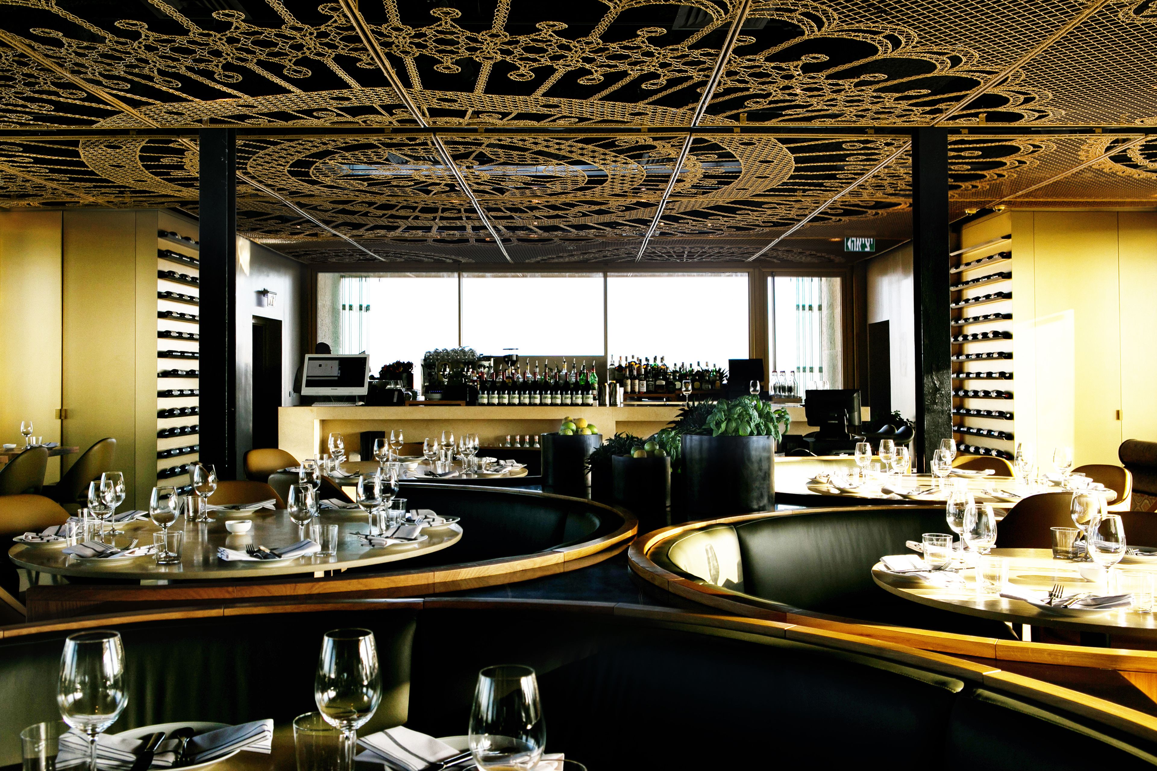 A restaurant with round tables set for dining, a bar area with bottles, and a ceiling with intricate designs.