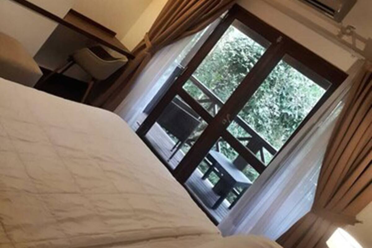 Una habitación de hotel con cama, televisión, lámpara, aire acondicionado y ventana con cortinas.