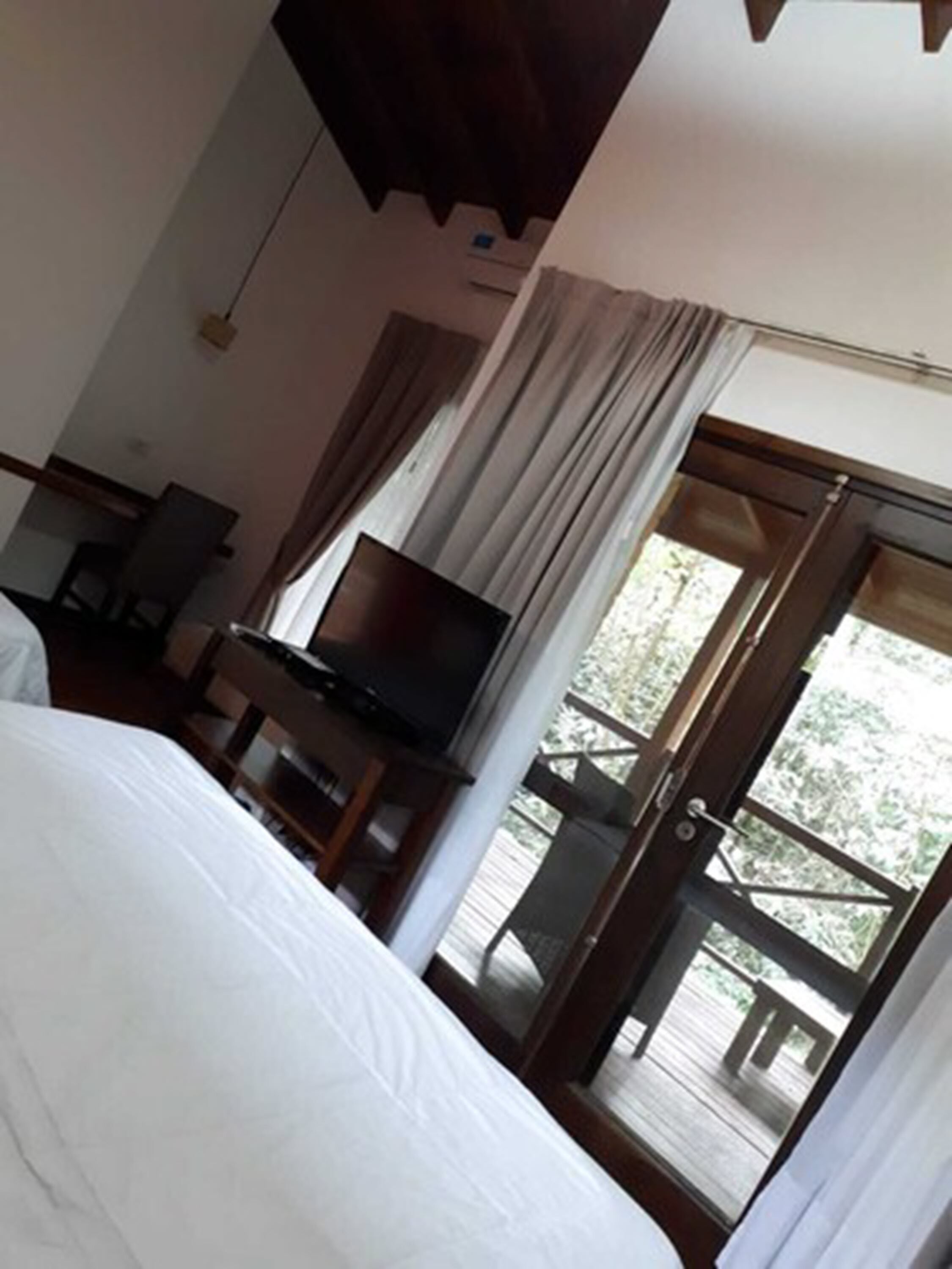 Een hotelkamer met een bed, een televisie, een bureau en een balkon met uitzicht op groen.