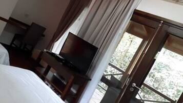Een hotelkamer met een bed, een televisie, een bureau en een balkon met uitzicht op groen.