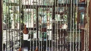 Une pièce dotée d’une grande fenêtre, d’un plancher en bois et d’une décoration suspendue composée d’objets en bois et de perles.