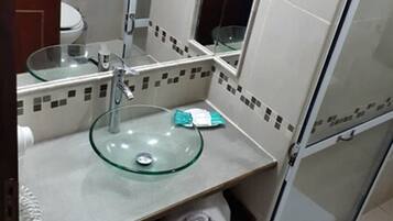 Un baño con un lavabo de vidrio, un inodoro y una zona de ducha.