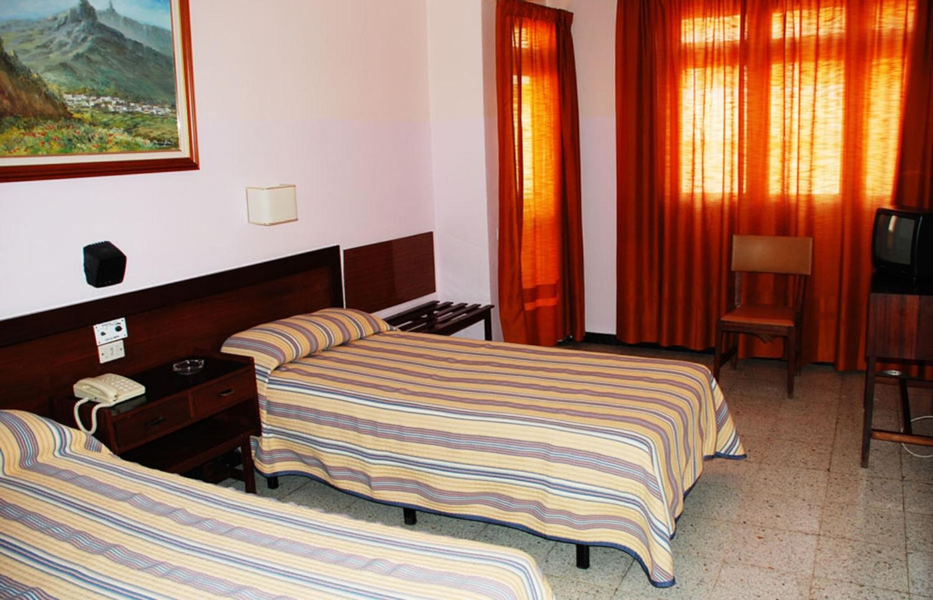 Una habitación de hotel con dos camas, un escritorio, una silla y un cuadro en la pared.