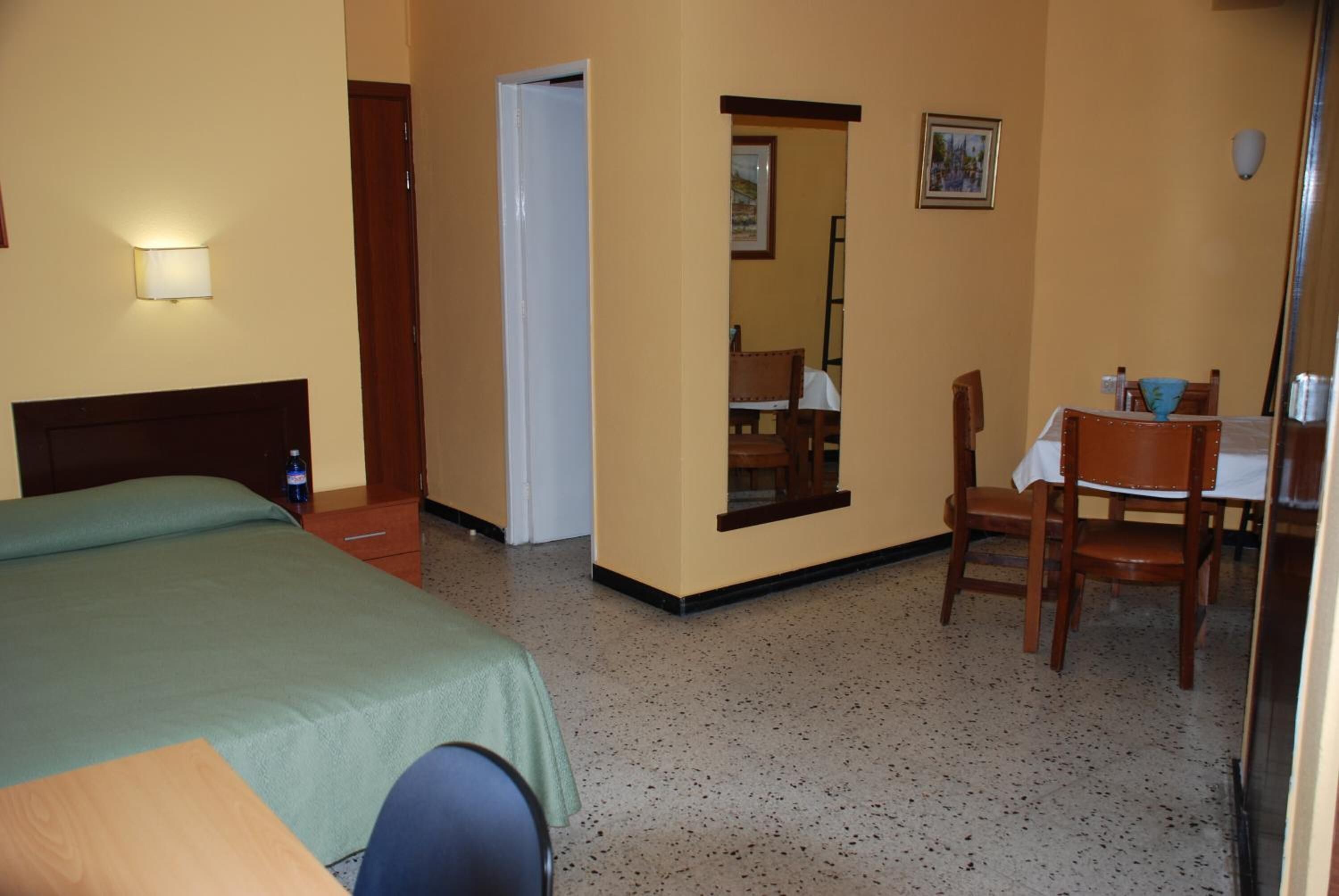 A hotel room with a bed, a desk, and a chair. There is a door leading to another room.