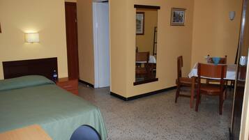 A hotel room with a bed, a desk, and a chair. There is a door leading to another room.