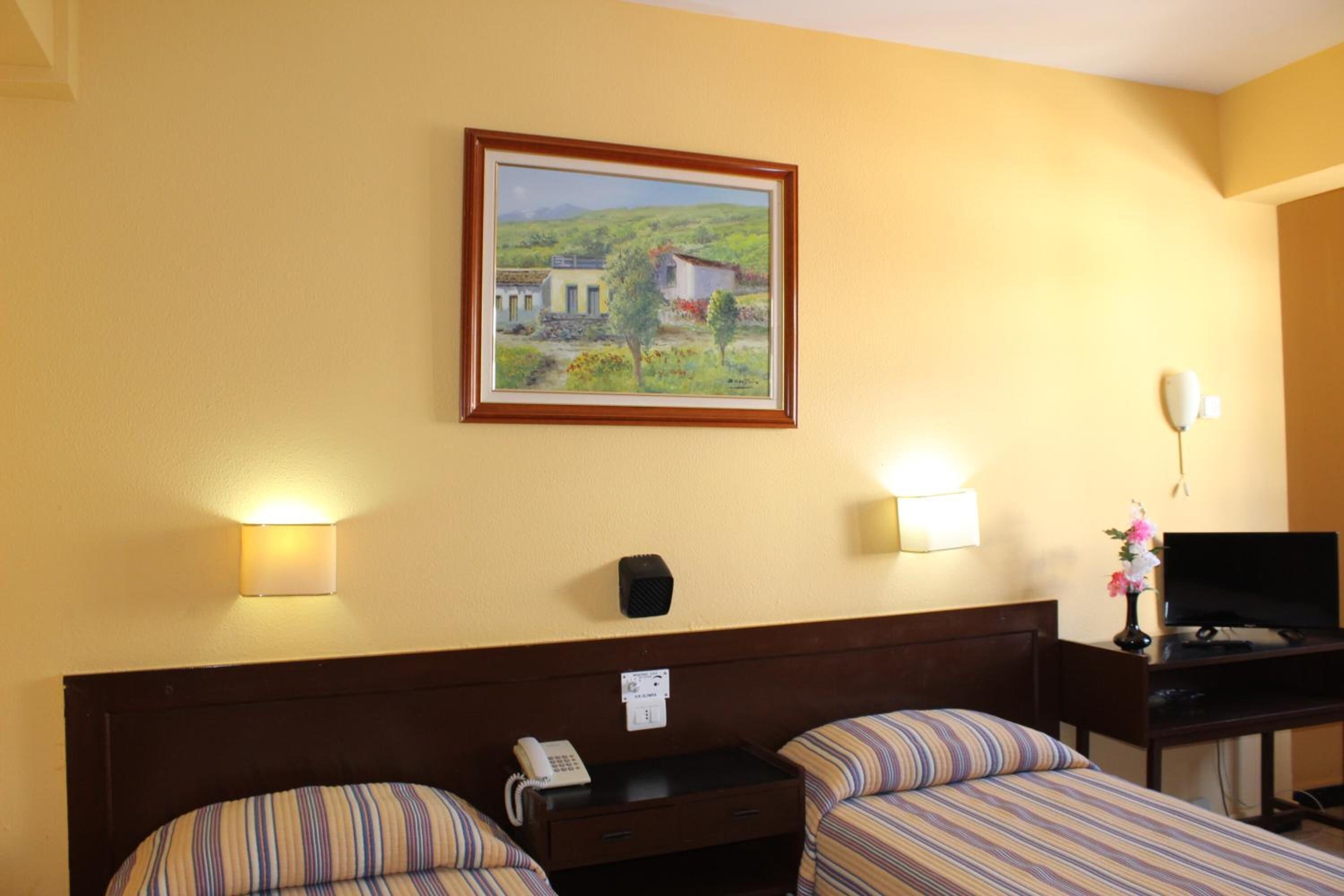 A hotel room with two beds, a desk with a television, a painting on the wall, and bedside lamps.