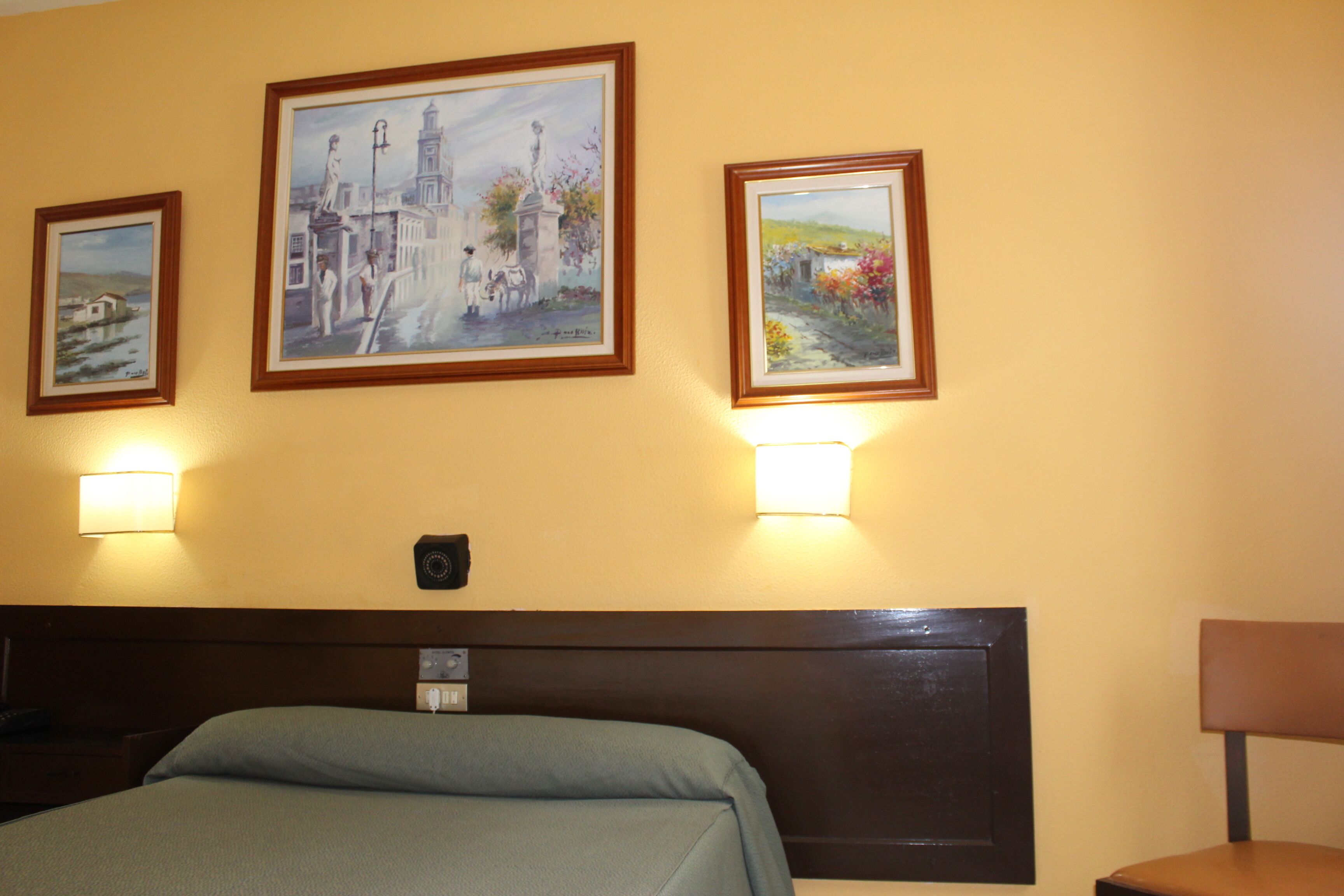 A hotel room with a bed, a headboard, and three framed paintings on the wall.