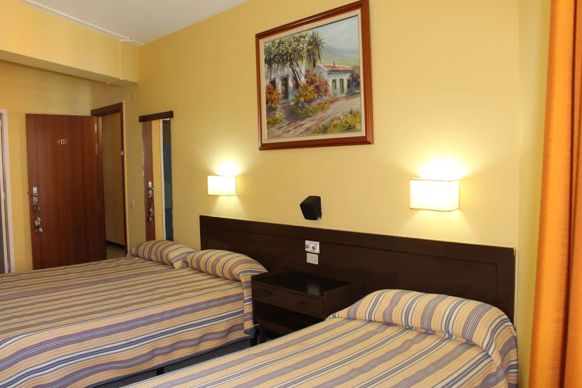 A hotel room with two beds, a painting on the wall, and two wall-mounted lamps.