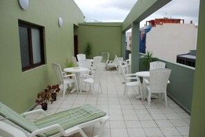 A rooftop patio with white plastic chairs and tables, a green wall, and a window. - Hotel Olympia (Las Palmas de Gran Canaria)