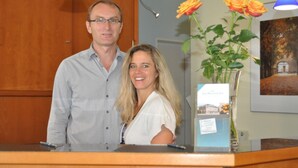 A reception desk with a man and a woman standing behind it, a vase with roses, and a framed picture on the wall. - Hotel zum Deutschen Eck (Meerbusch)