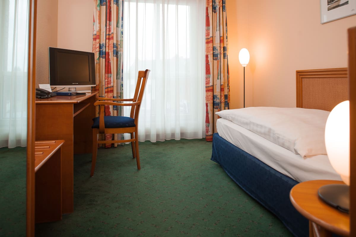 Ein Hotelzimmer mit einem Bett, einem Schreibtisch mit Computer, einem Stuhl und einer Lampe.
