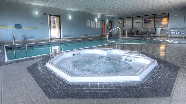 A swimming pool with a hot tub, tiled walls, and a clear glass door. - Holiday Inn Express & Suites Toronto Airport West by IHG (Mississauga)