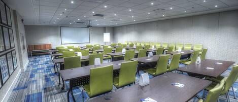 A conference room with multiple tables and chairs, a projector screen, and a whiteboard.