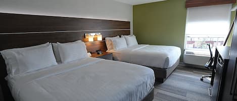 A hotel room with two beds, a nightstand with a lamp, a desk, and a window with a view.
