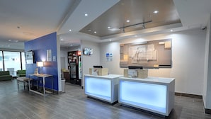 A modern hotel reception area with two illuminated reception desks, a blue accent wall, and a television screen. - Holiday Inn Express & Suites Toronto Airport West by IHG (Mississauga)