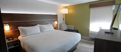 A neatly made bed with white linens, a wooden headboard, bedside lamps, a small bedside table with a clock, and a desk with a remote control.