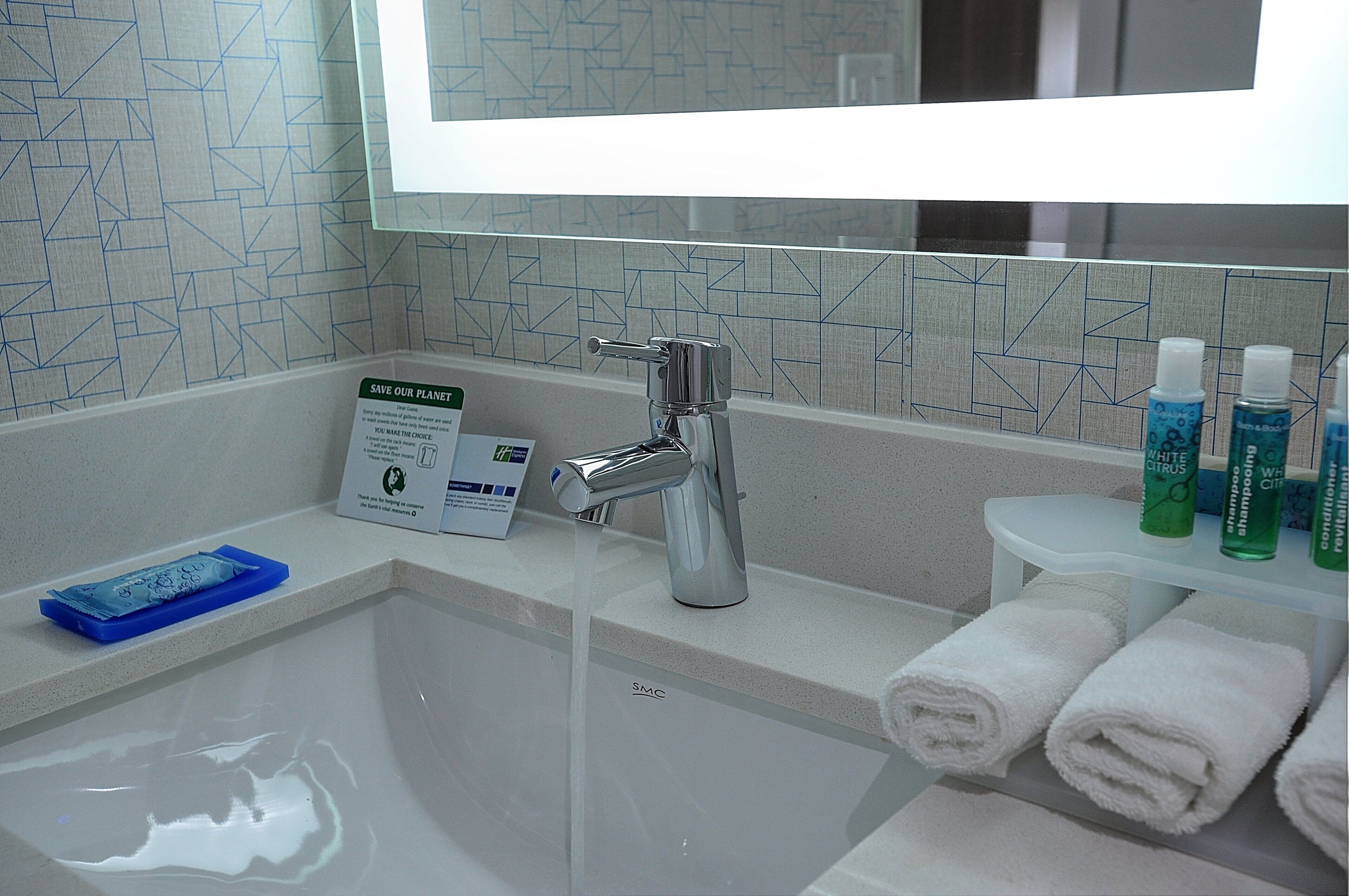 Un baño con un lavamanos moderno, un espejo y un estante con artículos de aseo.