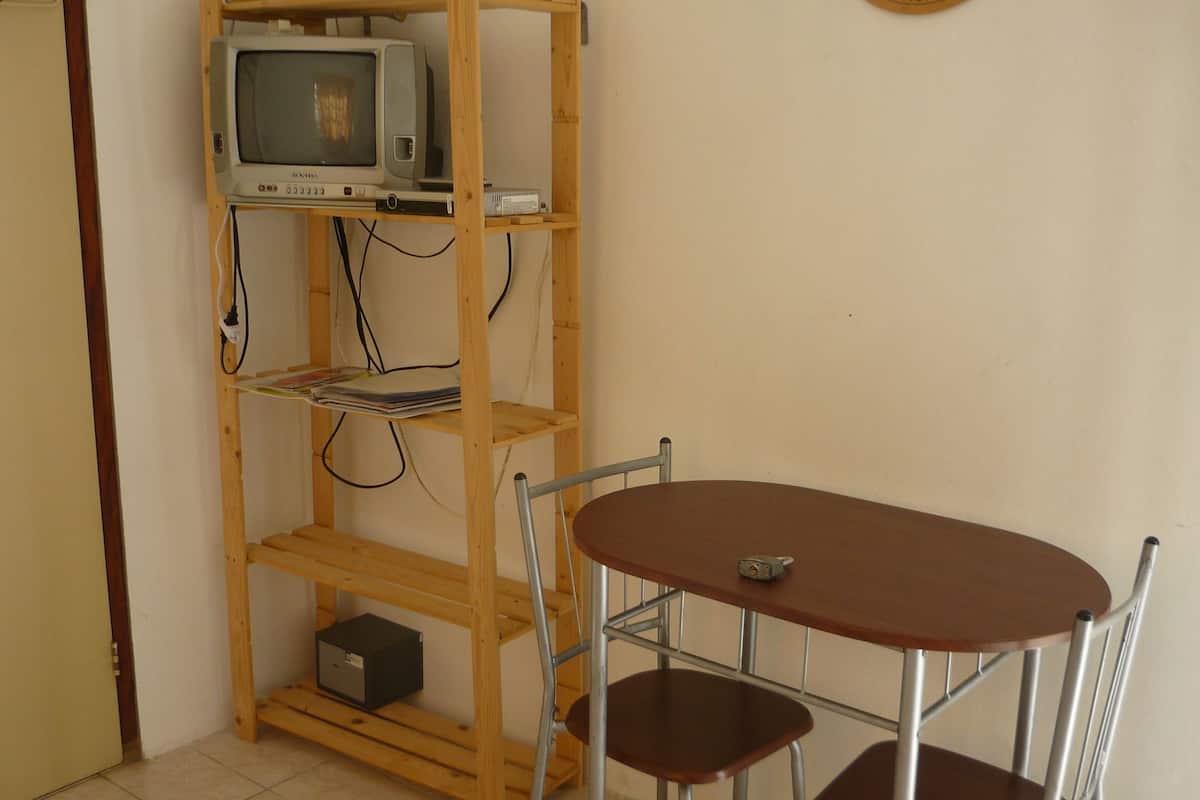 A room with a wooden TV shelf, a table with two chairs, and a small black box on the floor.
