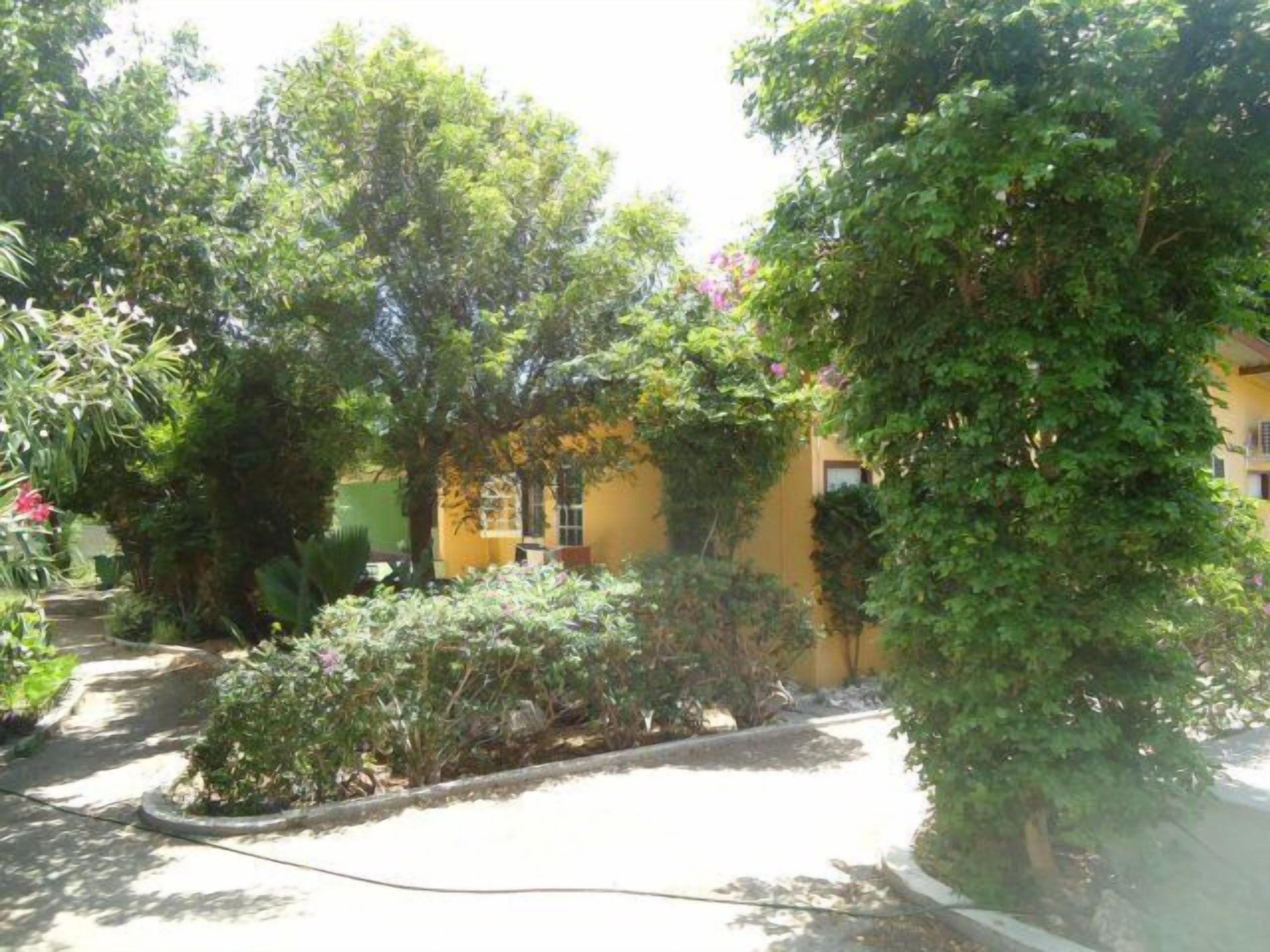 A yellow building surrounded by lush greenery and a paved pathway.