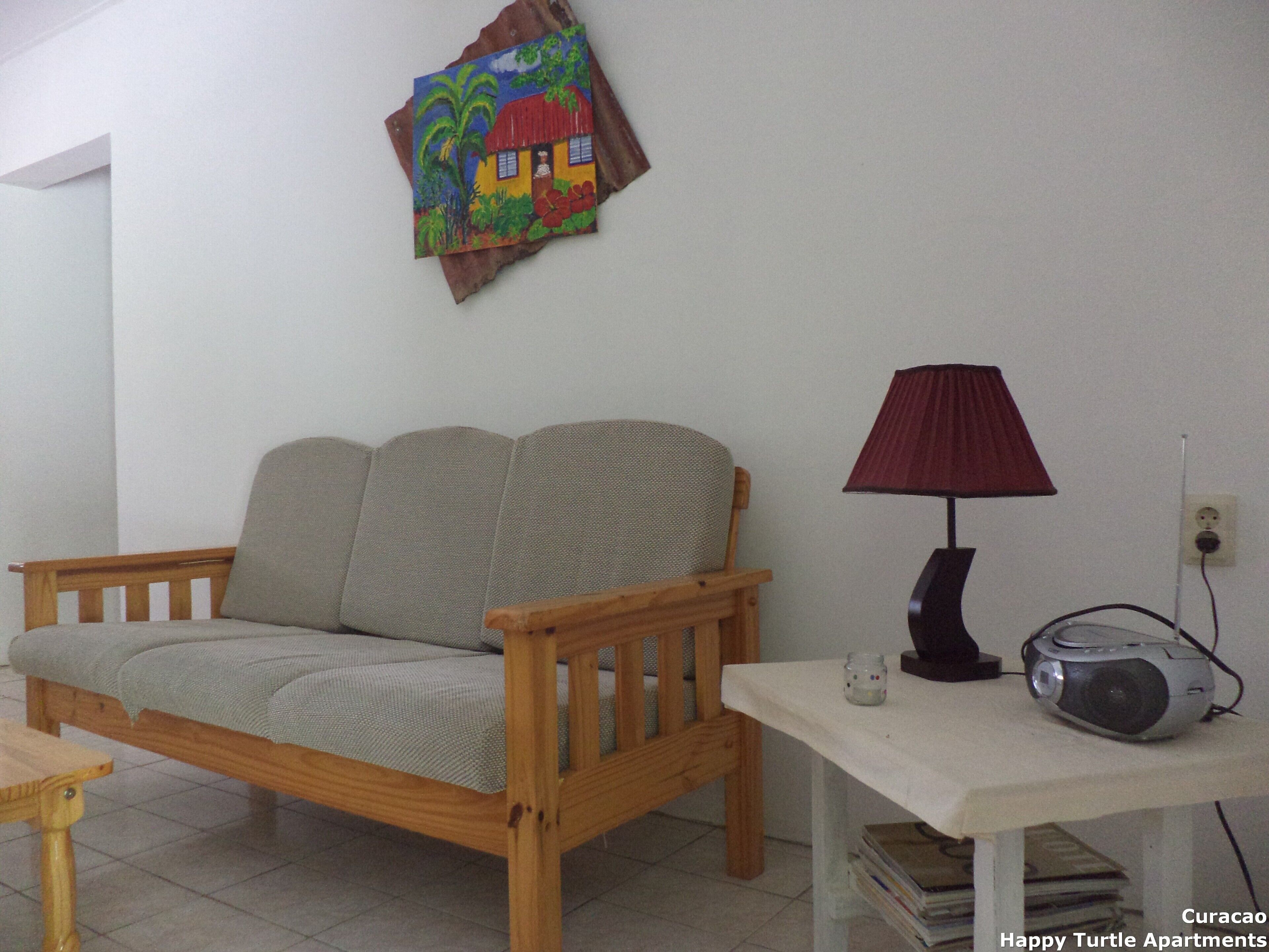 A room with a wooden sofa, a small table with a lamp, and a painting on the wall.