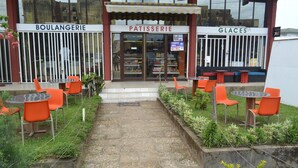 Un espace extérieur aménagé avec des tables et des chaises, situé devant une boulangerie, une pâtisserie et un magasin de glaces.
