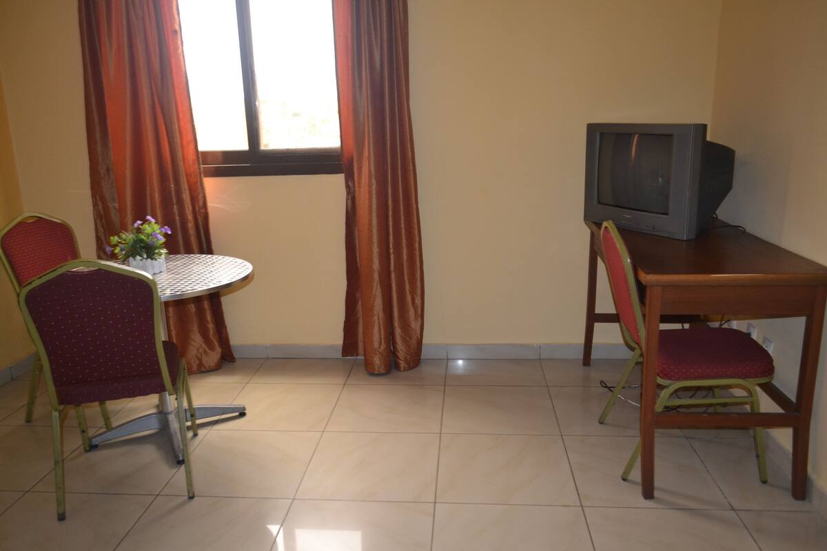 A small room with a round table, two chairs, a television, and a window with curtains.