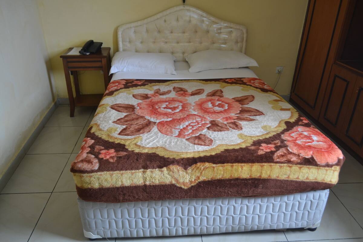 A bed with a floral bedspread, a bedside table with a phone, and a nightstand.