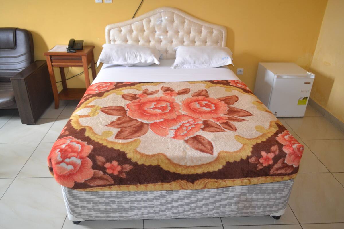 A bed with a floral bedspread, a white headboard, and a small bedside table with a phone.