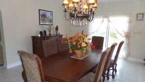 Une salle à manger avec une table en bois, six chaises, un lustre et un vase de fleurs.