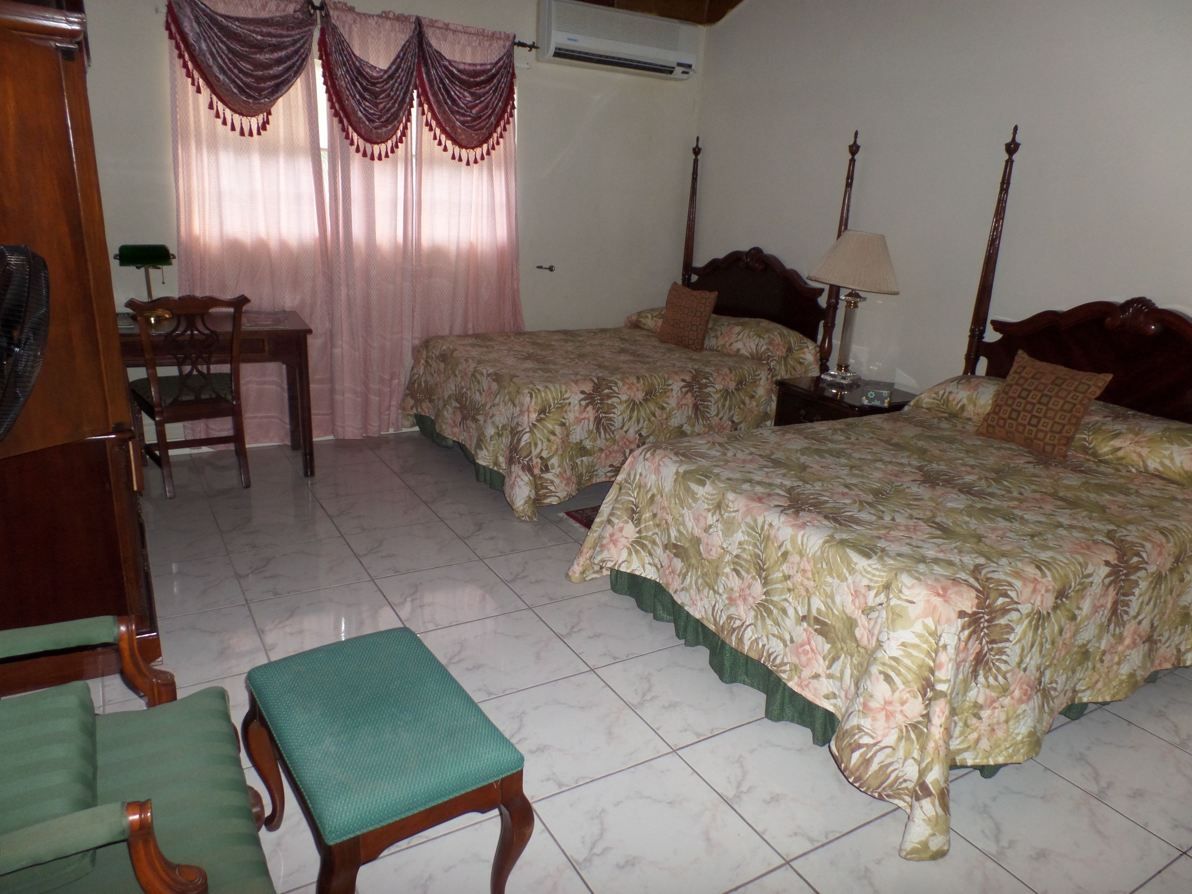 A hotel room with two beds, a desk, a chair, and a window with curtains.