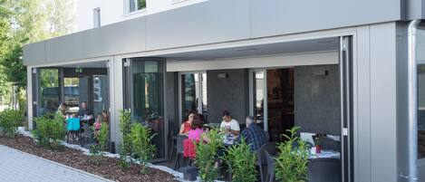 An outdoor seating area with tables and chairs, surrounded by small plants and a pathway.
