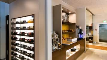 Zona de recepción de un hotel con una estantería de vinos, mesa de buffet y máquina de café.