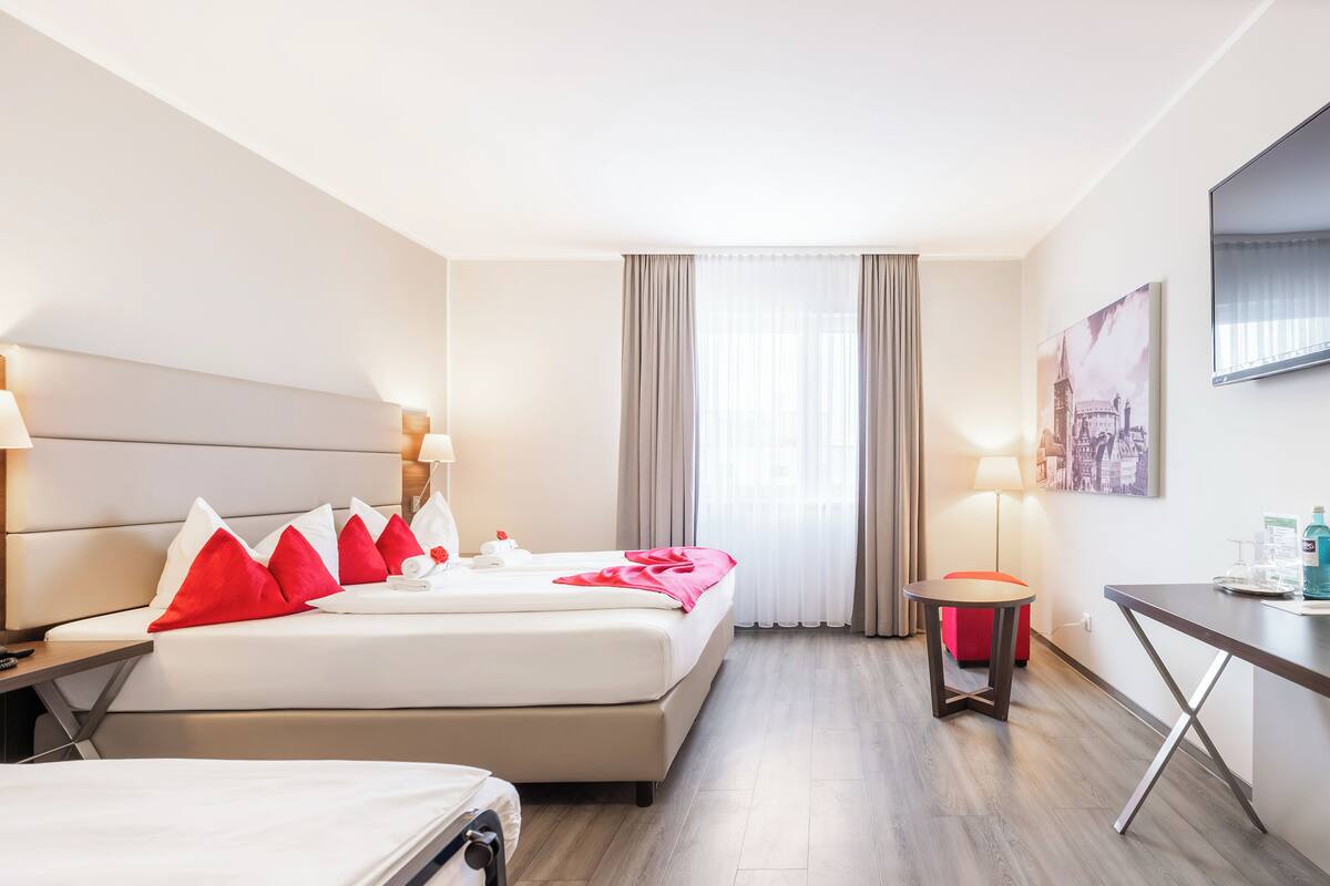 Ein Hotelzimmer mit Bett, Nachttischen, Schreibtisch und einem fenster mit Vorhängen.