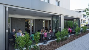 Ein Sitzbereich im Freien mit Tischen und Stühlen, umgeben von einer niedrigen Steinmauer und kleinen Pflanzen.