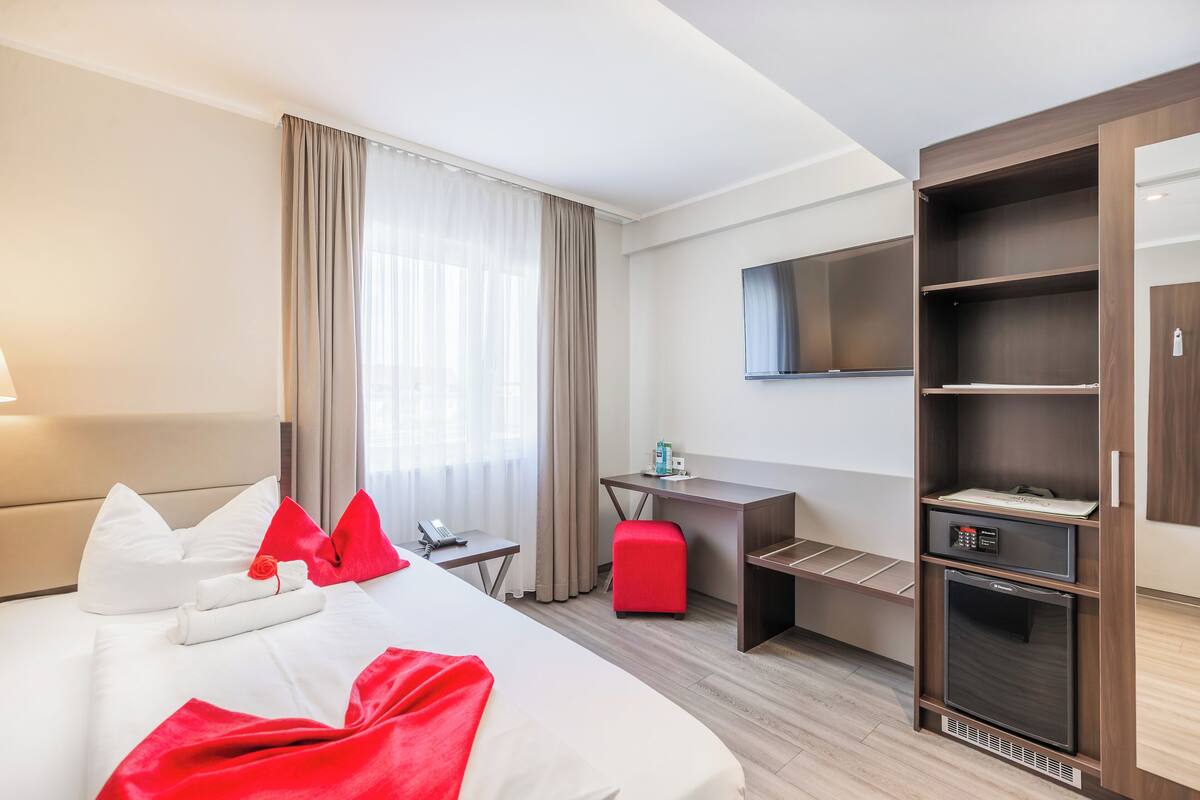 Ein Hotelzimmer mit Bett, Schreibtisch, Stuhl, Fernseher, Minibar und Kleiderschrank.
