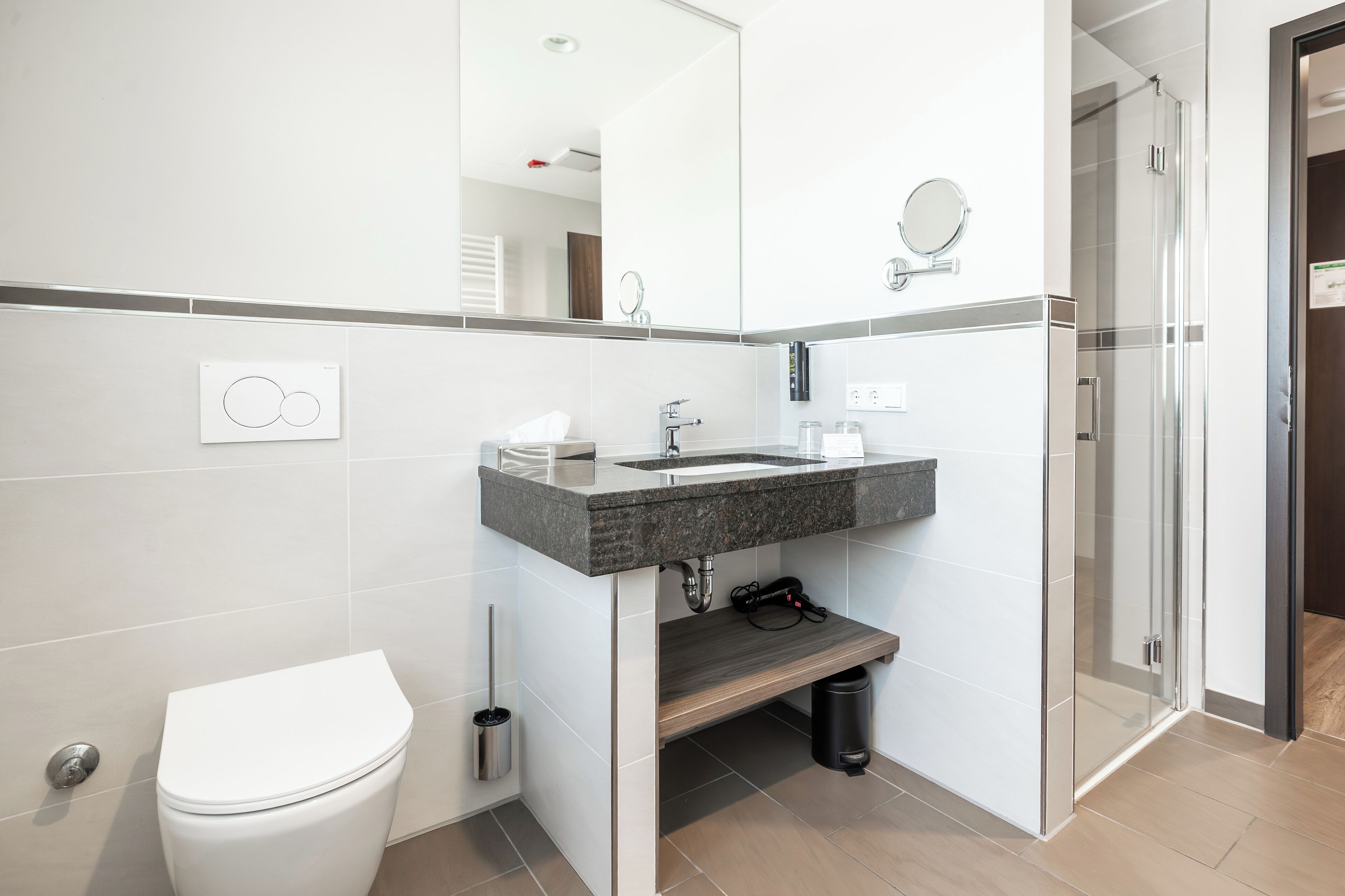 Een moderne badkamer met een wit toilet, een granieten wastafel, een spiegel en een douche.