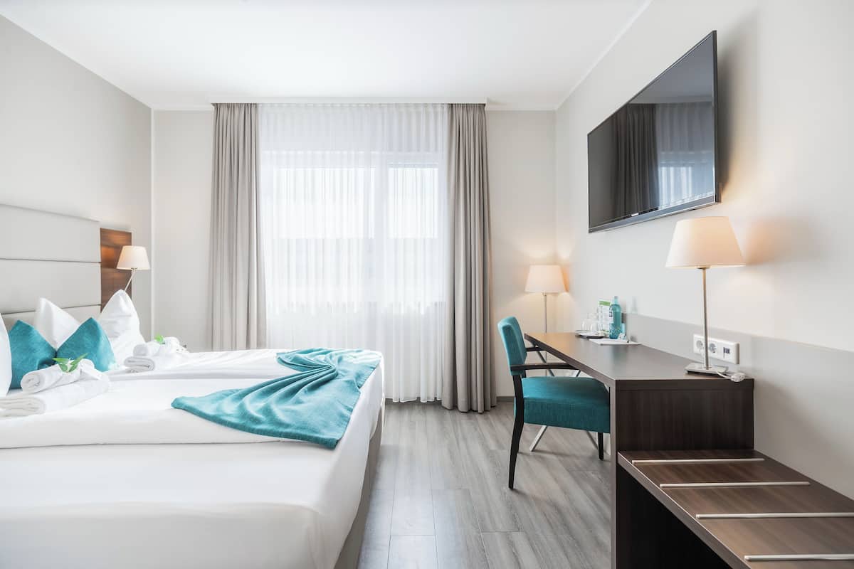 Ein Hotelzimmer mit Bett, Schreibtisch, Stuhl, Fernseher und Vorhängen.